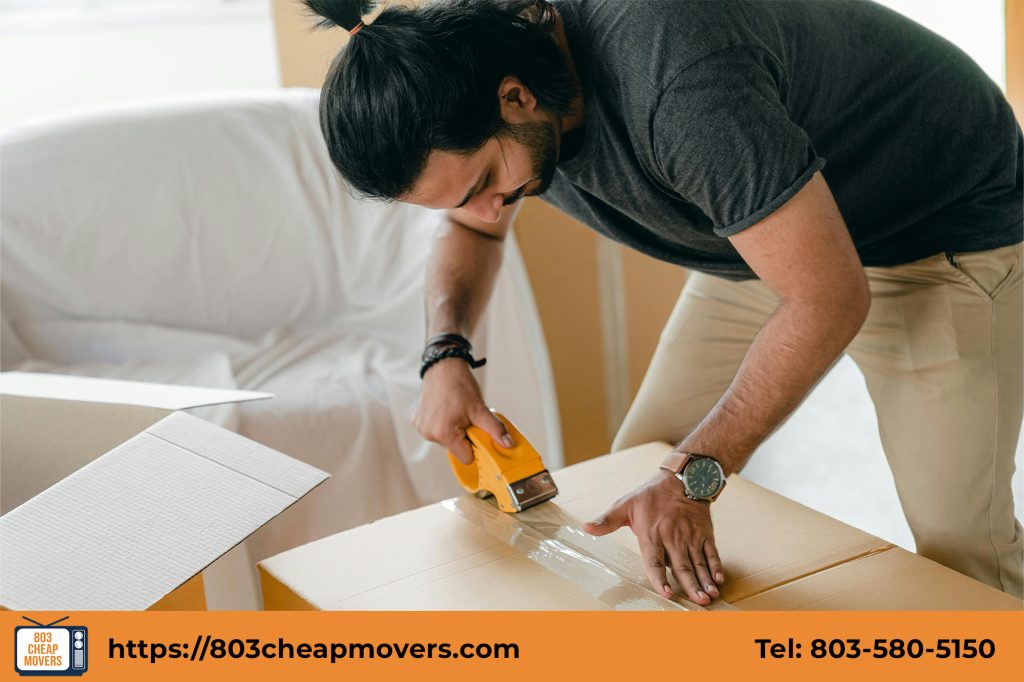 A man packing boxes with tape, preparing to move into a new home.